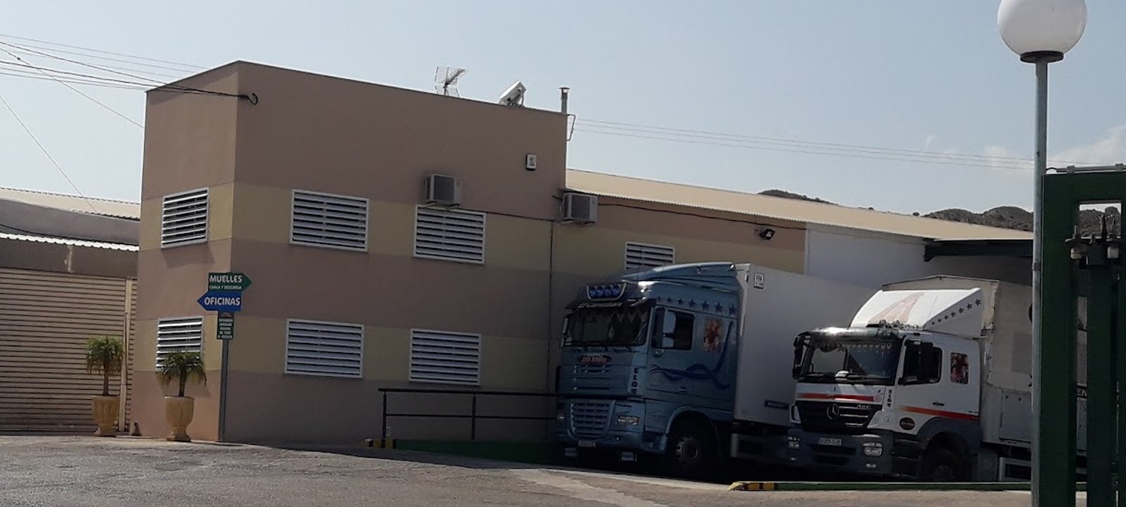Fachada del edificio de oficinas de Frutas Sergio con la señal de muelles y oficinas, y dos camiones cargando